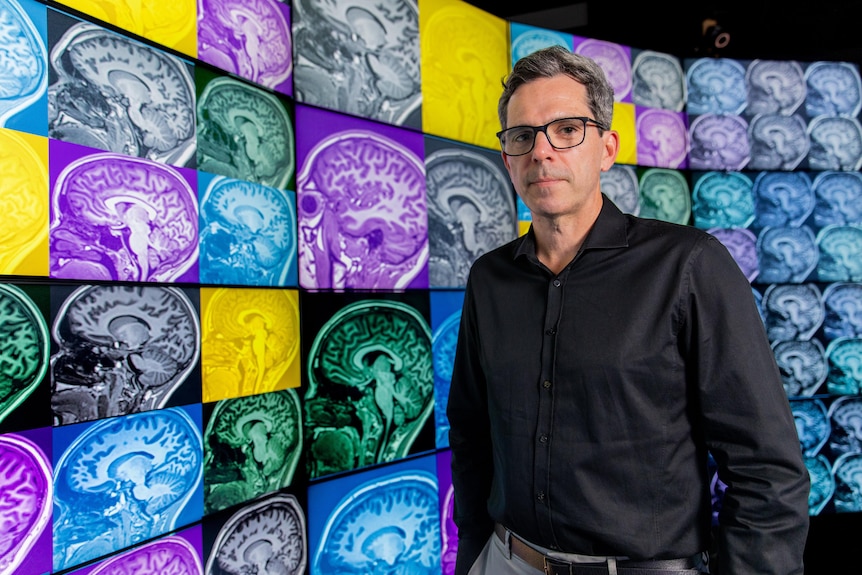 Dan Hermens stands in front of a wall of brain images