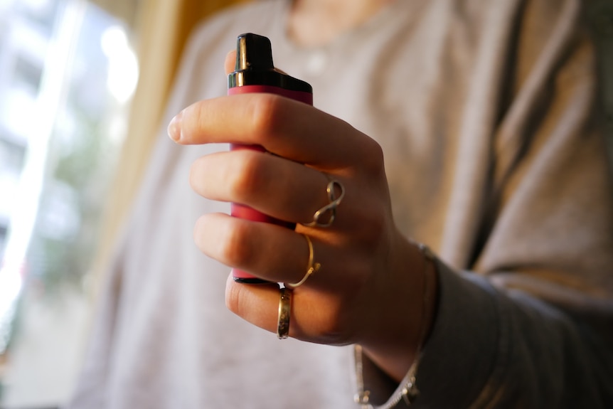 A picture of a teenager's hand holding a vape.