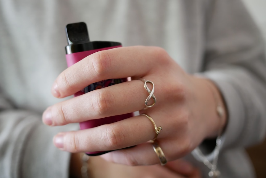 A hand holding a pink vape